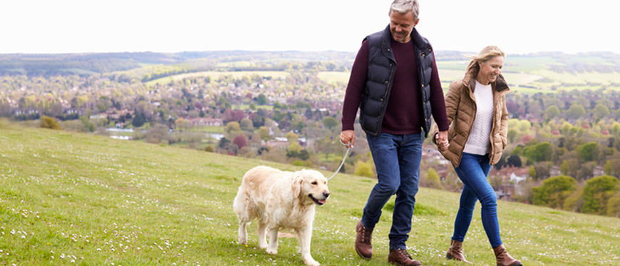 Older couple walking dog in field with hills in background