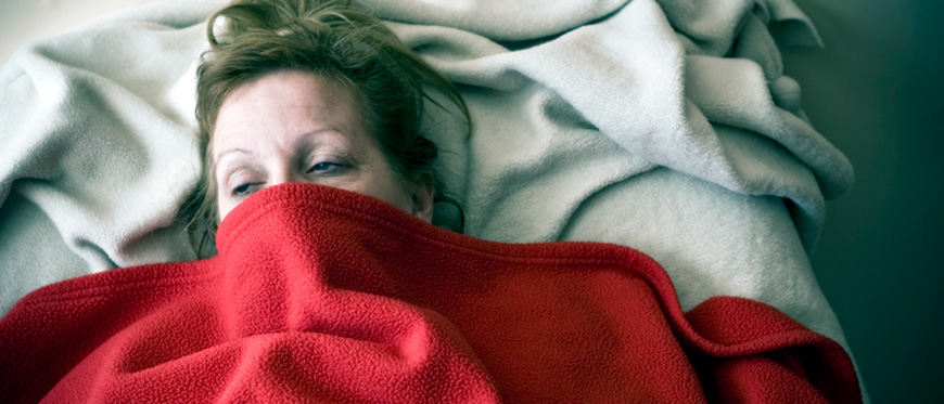 Woman in bed sick with face partially covered by blanket