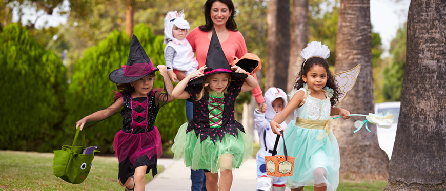 Three girls dressed in witch and princess costumes trick or treating with their mom