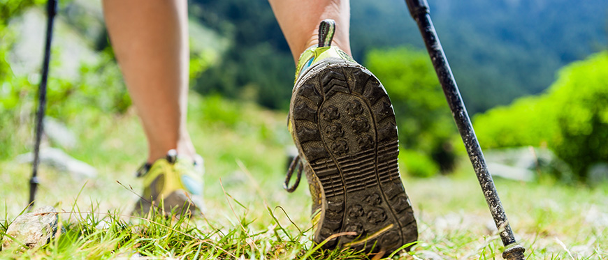 Close up of girl's legs and muddy sneakers hiking with poles