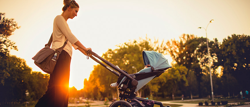 Woman pushing a stroller with sun setting