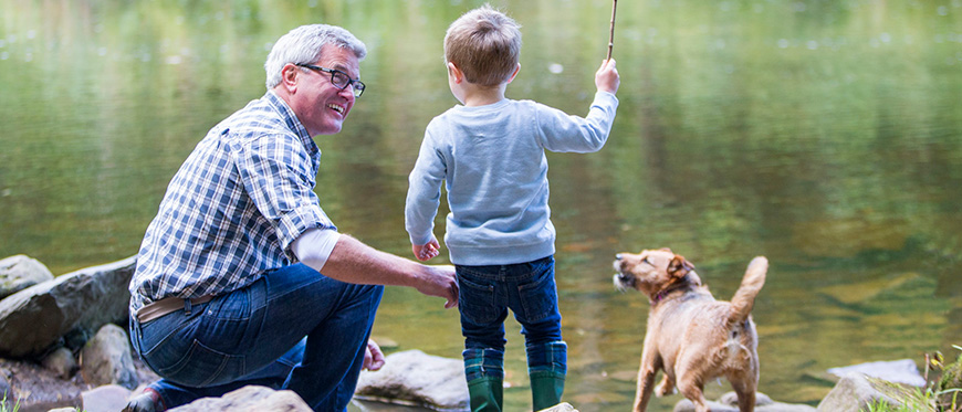 Grandfather playing with grandson and dog by a river