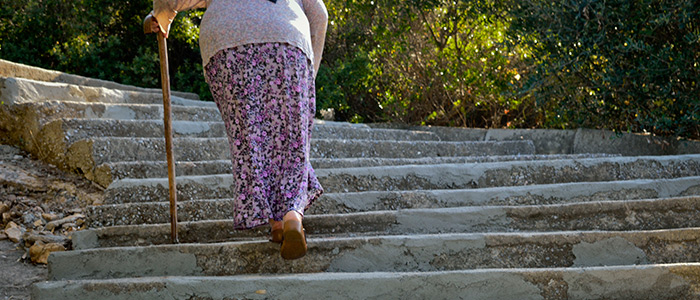 Older woman walking up flight of stone steps using cane