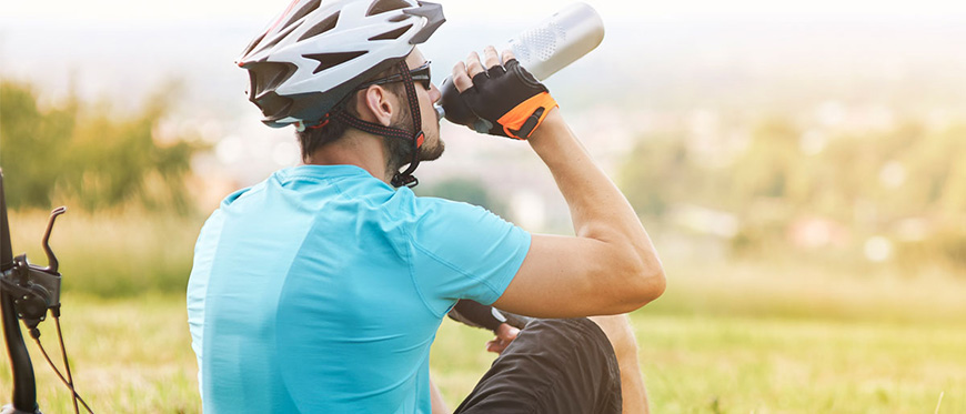 Male cyclists sitting next to bike drinking water from water bottle