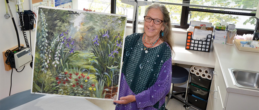 Andrea Triguba, RN holding up a ceiling tile she painted of a garden