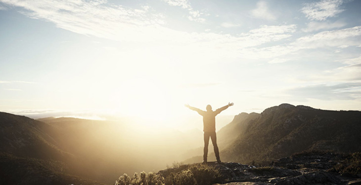 Man standing with arms out at top of mountain at sunrise