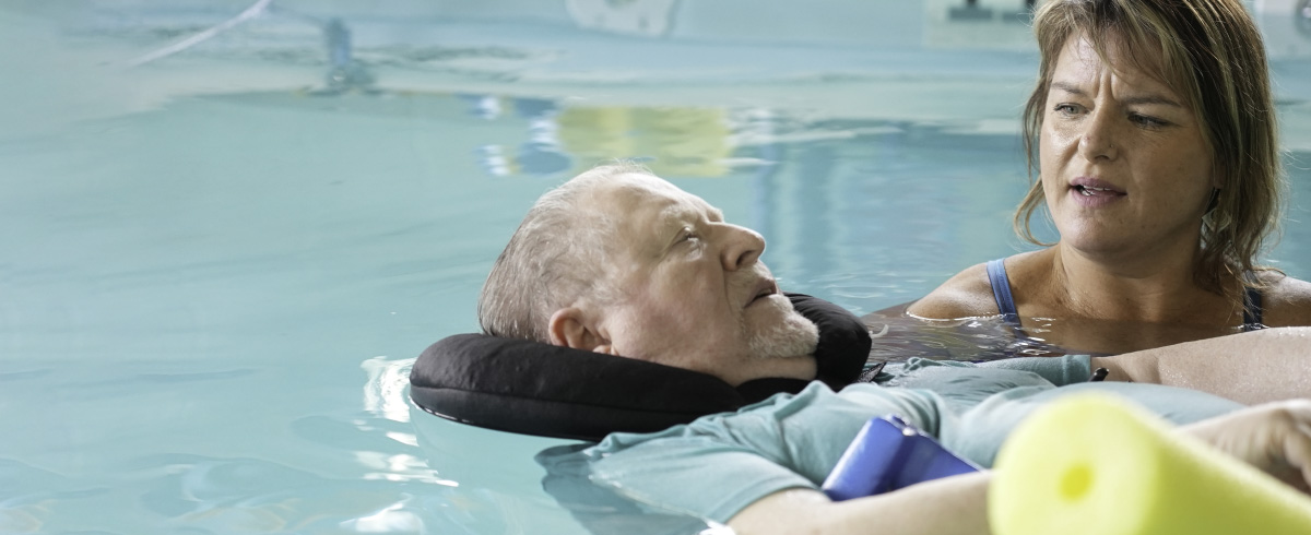 Physical therapist doing aquatic therapy with older man in pool