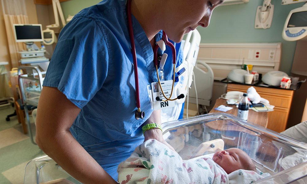 Nurse returning newborn to crib in new mom's private room